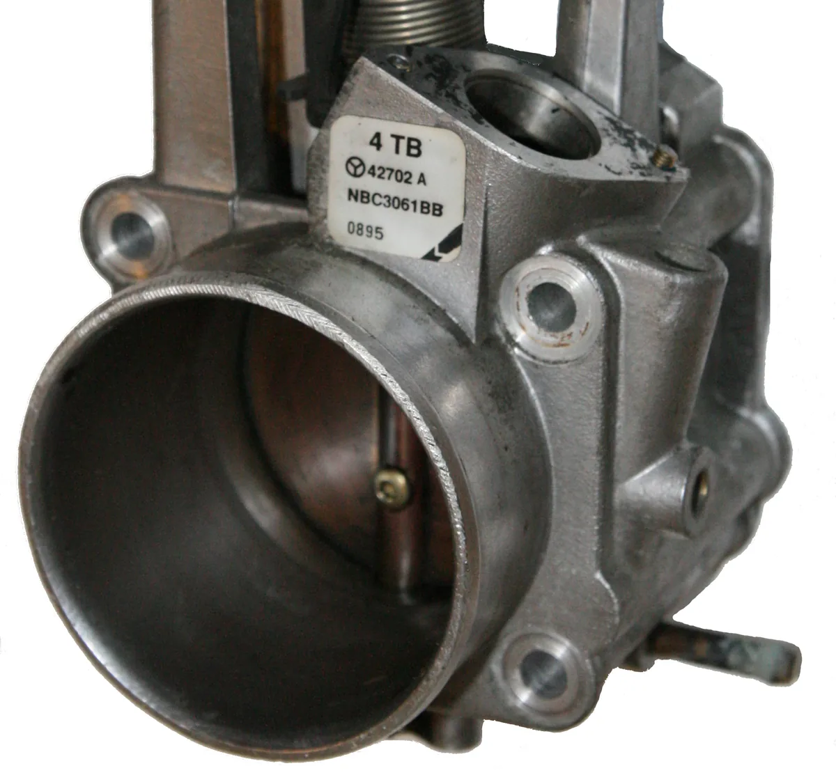 A metal throttle body with a wide round bore, a label and bolt holes, on a white background