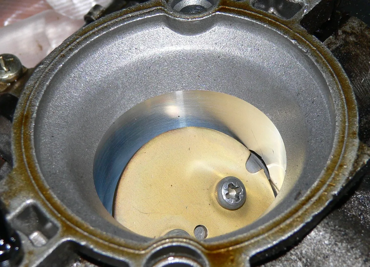 Looking into a throttle body bore at the round metal plate that opens and closes it, with oily residue