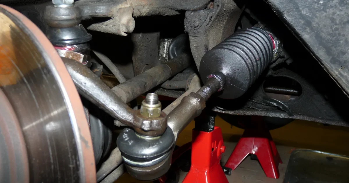 A new outer tie rod end and the black rubber boot over the inner tie rod, next to the brake disc of a car standing on red jack stands