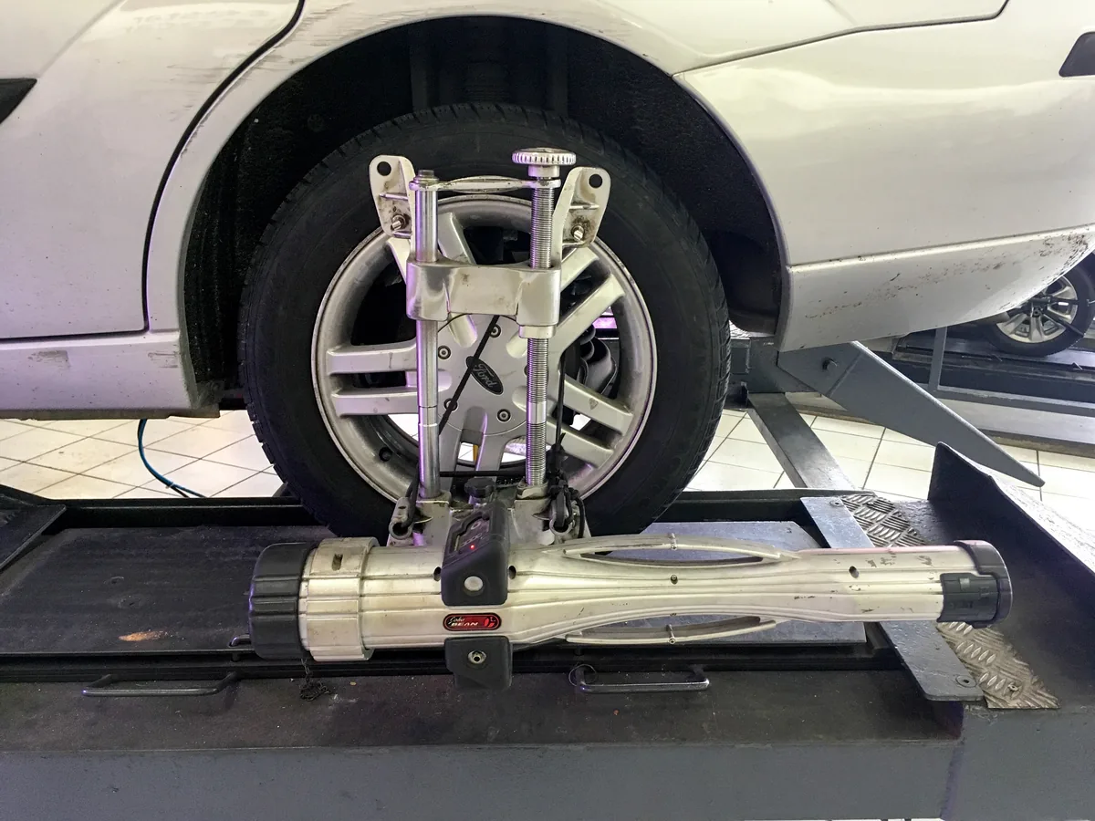 An alignment clamp fixed to the front wheel of a silver Ford Focus standing on an alignment rack