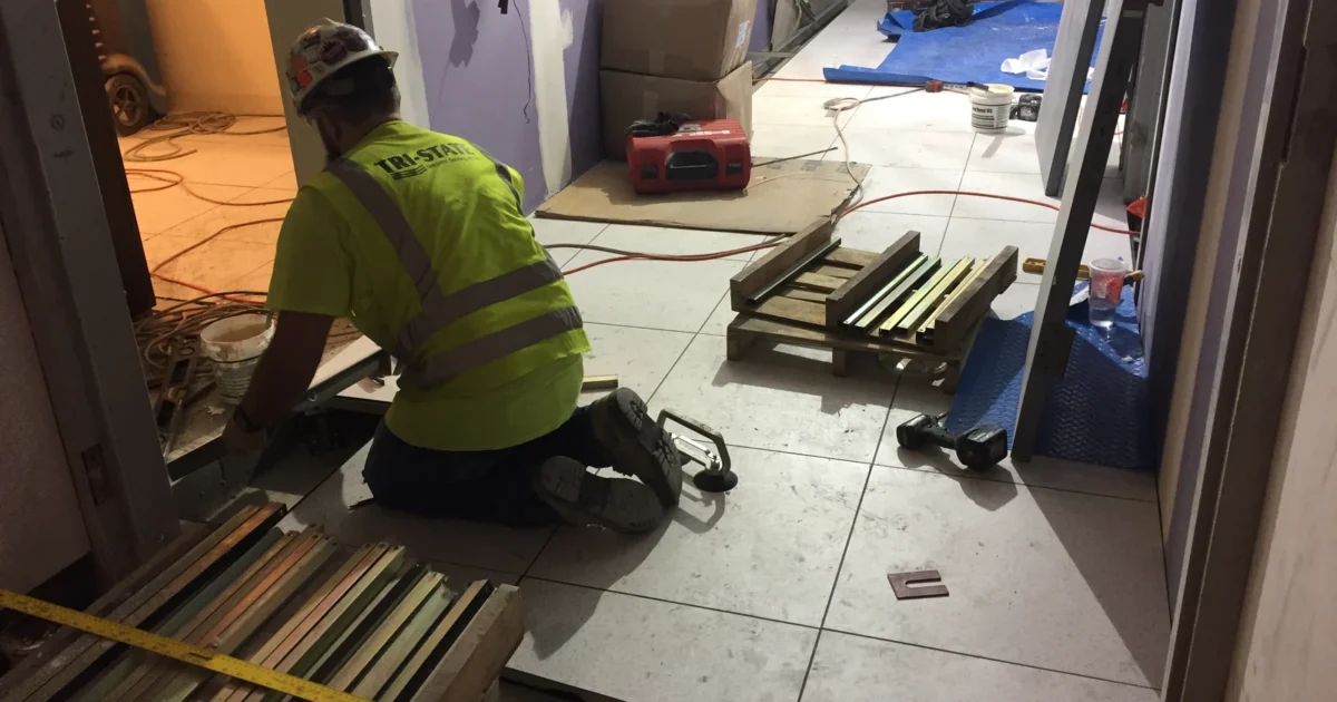 Worker kneeling beside newly laid floor tiles during construction of a Long Island Rail Road concourse.