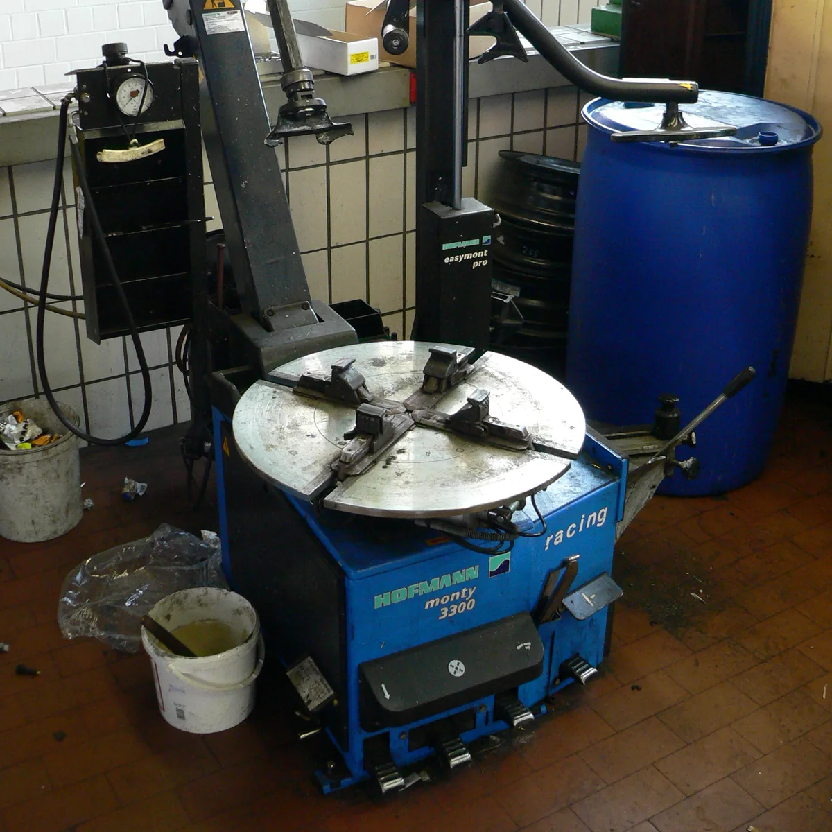 A blue tire changing machine with a round turntable in a small workshop, next to a blue drum