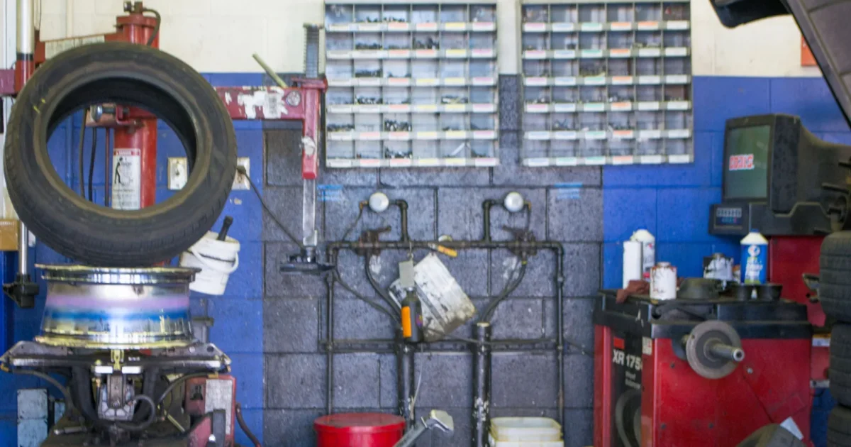 A car tire upright on a fitting machine among tools and service equipment in a workshop.