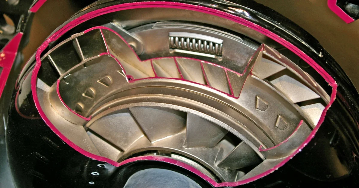 A museum torque converter cutaway exposes curved metal vanes and internal parts, with cut edges painted pink.