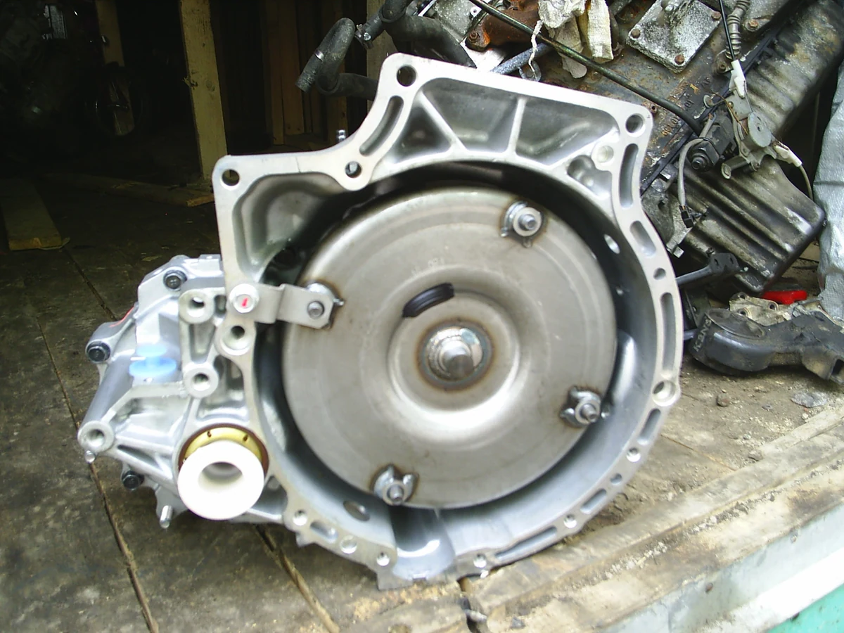 The round metal torque converter sits inside the open bellhousing of a removed 4EAT automatic transmission.