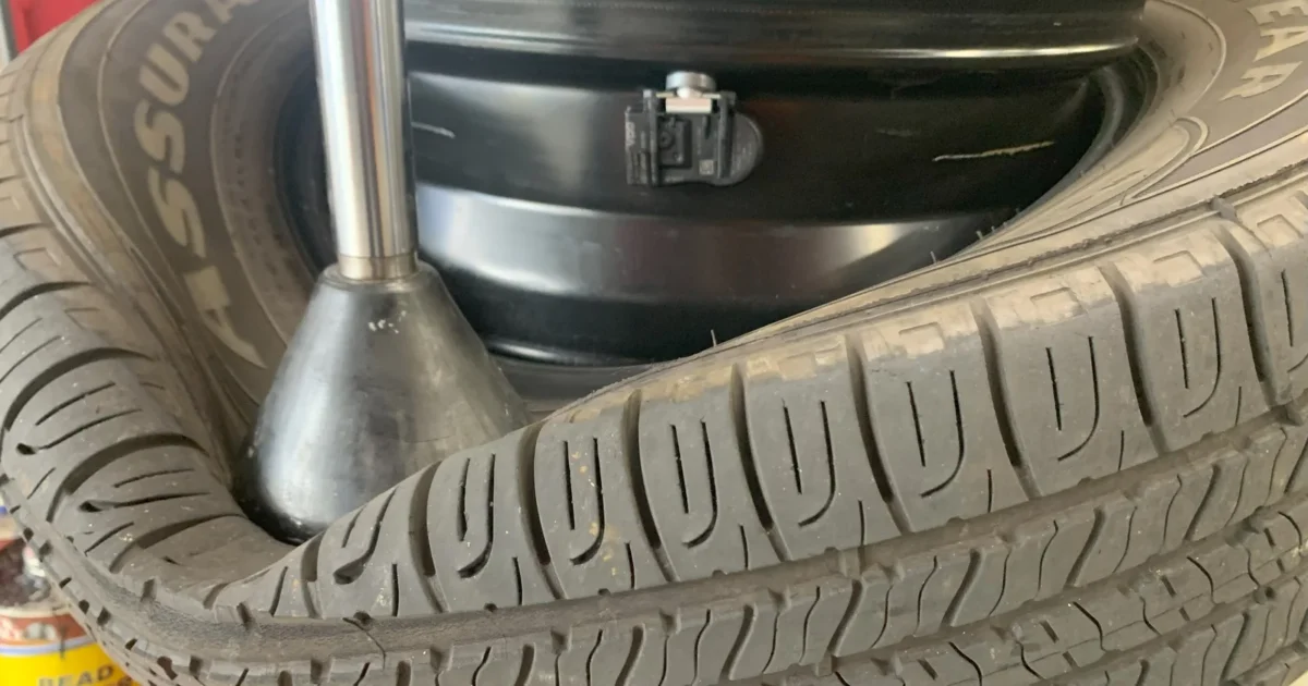 A black tire pressure sensor attached to the inner rim during tire work.