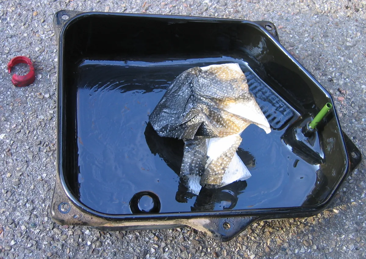 The black oil pan of an automatic transmission, taken off and drained, with dark oil sludge and a rag inside