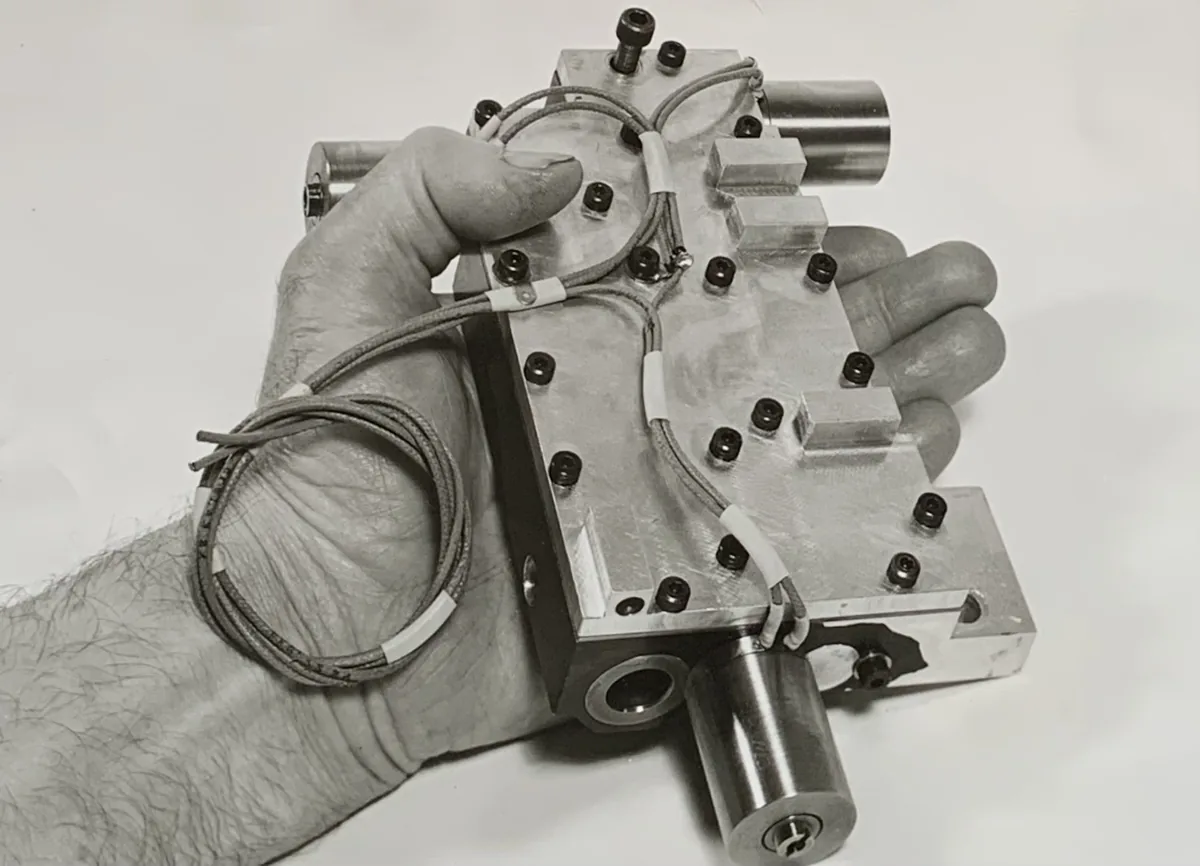 A hand holding a metal valve block for an automatic transmission, with solenoid valves and their thin wires