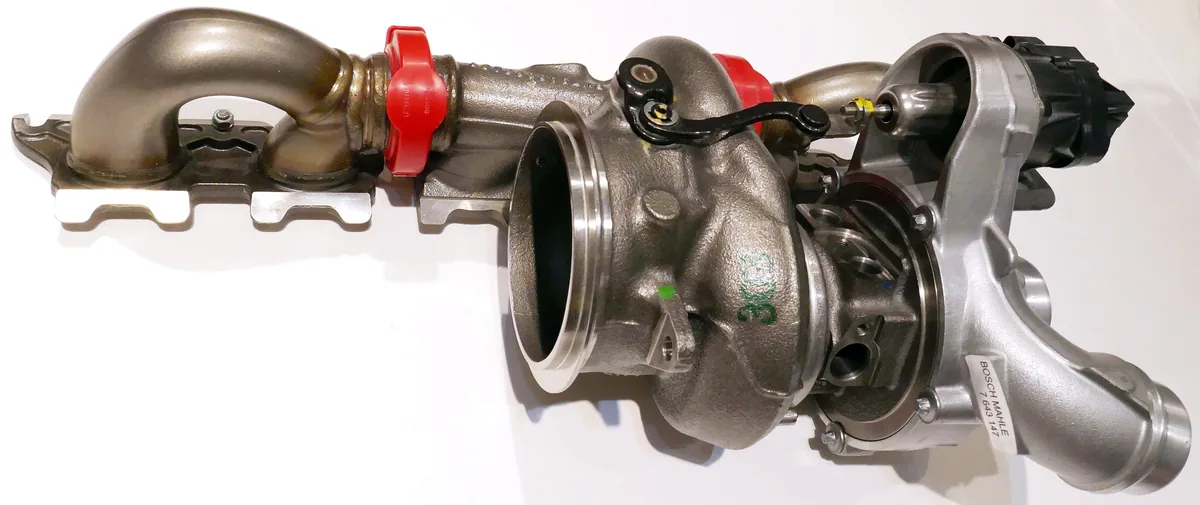 A modern car turbocharger joined to its exhaust manifold, with pipes and a small actuator, on a white background