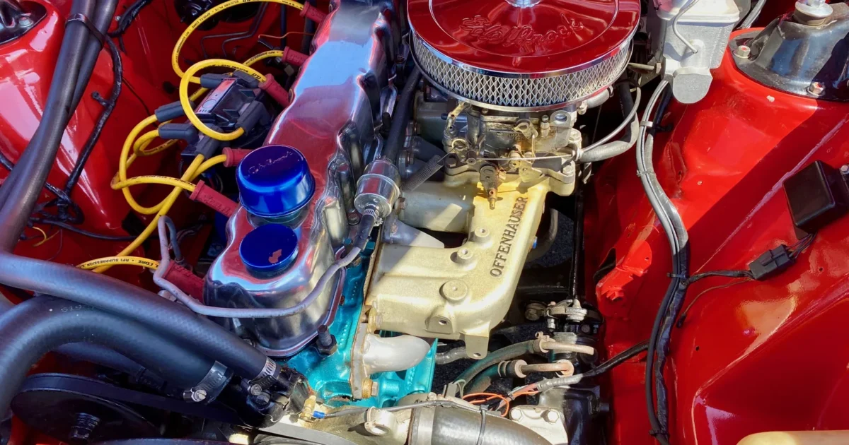 A red engine bay with a chrome air cleaner, a gold intake manifold and many black rubber hoses and wires