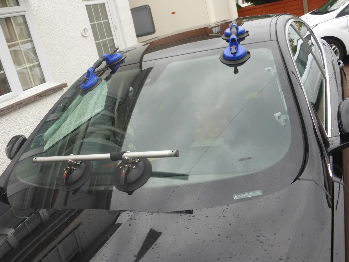 A black car with a new windshield held in place by blue suction cups while it is fitted